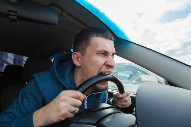 An unbalanced, goosey man bites a car steering wheel from anger  - Photo, Image