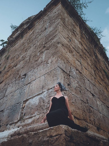 Vista de cerca de la hermosa joven y atractiva mujer musulmana en vestido negro largo de pie en la esquina de la torre Hidirlik
 - Foto, Imagen
