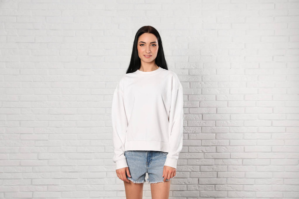 Portrait of young woman in sweater at brick wall. Mock up for design - Foto, afbeelding