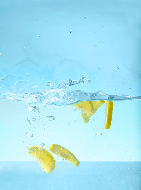 Water with lemon slices against blue background. Refreshing drink - Φωτογραφία, εικόνα