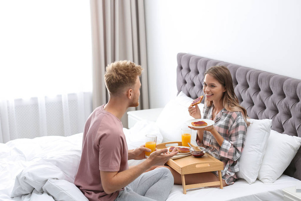 Happy young couple having romantic breakfast on bed at home - Foto, afbeelding
