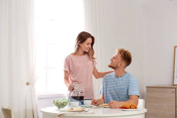 Happy young couple having breakfast at table in room - 写真・画像