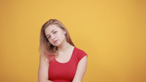νεαρή ξανθιά κορίτσι με κόκκινο μπλουζάκι πάνω από απομονωμένο πορτοκαλί φόντο δείχνει τα συναισθήματα - Πλάνα, βίντεο