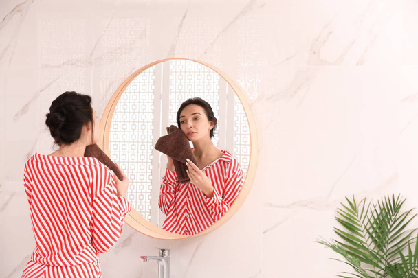 Young woman with towel near mirror in bathroom - Zdjęcie, obraz