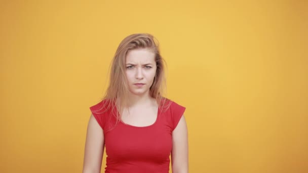 νεαρή ξανθιά κορίτσι με κόκκινο μπλουζάκι πάνω από απομονωμένο πορτοκαλί φόντο δείχνει τα συναισθήματα - Πλάνα, βίντεο