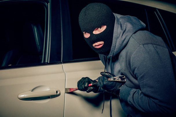 άντρας κλέφτης θα ανοίξει την πόρτα του αυτοκινήτου με ένα λοστό. - Φωτογραφία, εικόνα