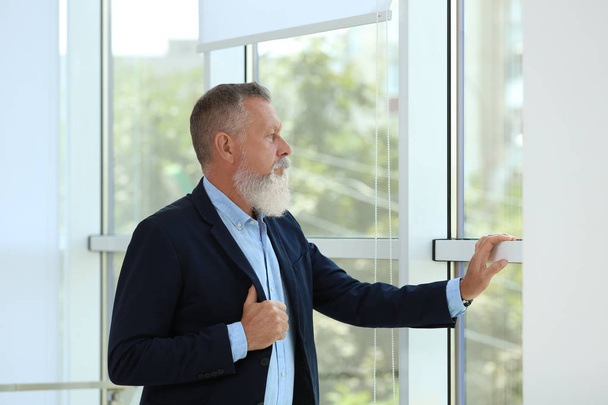Portrait of handsome mature man in elegant suit looking out window indoors - Photo, image
