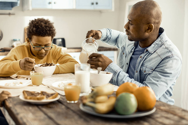 Dziecko wybiera mleko na śniadanie, a tata nalewanie mu szklankę. - Zdjęcie, obraz