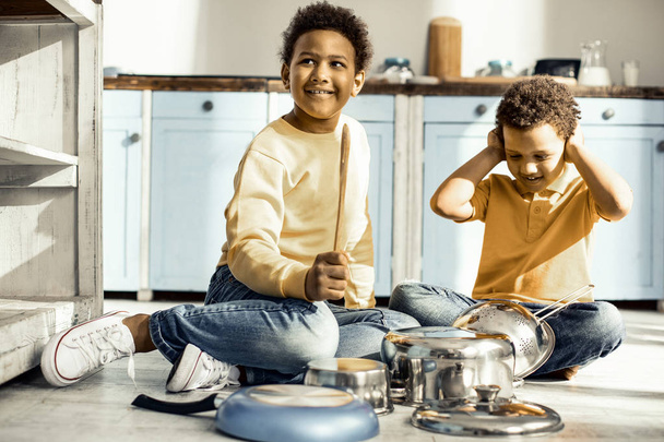 Boy covering ears while his brother trying to play on the dishes. - Fotoğraf, Görsel