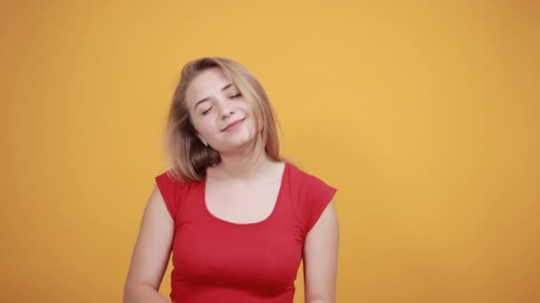 Jong blond meisje in rood t-shirt over geïsoleerde oranje achtergrond toont emoties - Video