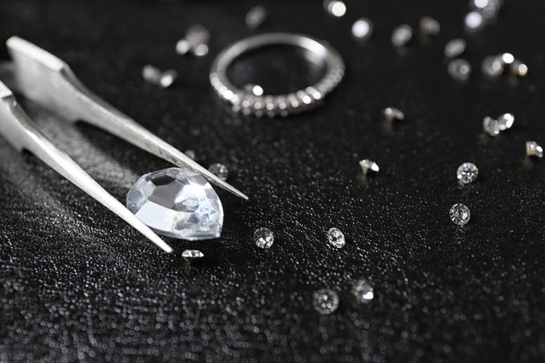 Jewels and tweezers on black leather surface - Photo, image