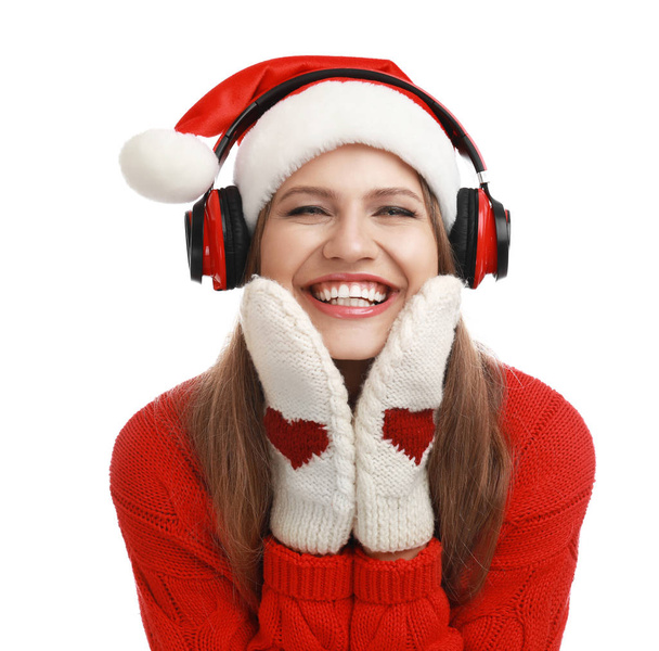 Young woman in Santa hat listening to Christmas music on white background - Фото, изображение