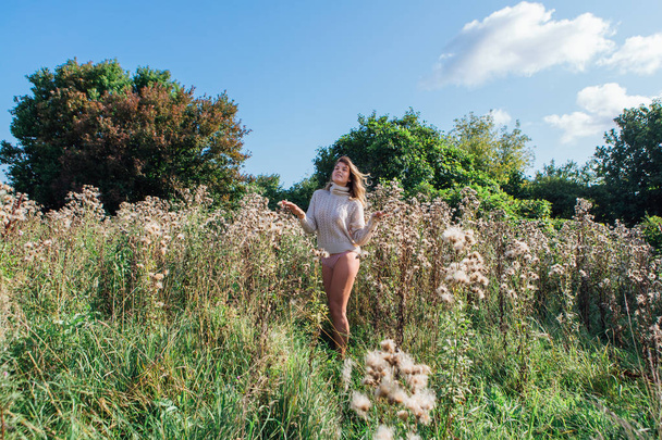 Happy young beautiful woman in sweater and underpants walking with bare foot in a field of dry agrimony - Fotografie, Obrázek