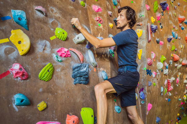 Muscular man practicing rock-climbing on a rock wall indoors - Фото, зображення