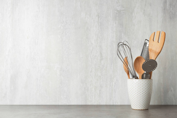 Тримач з кухонним посудом на сірому столі на світлому фоні. Простір для тексту
 - Фото, зображення