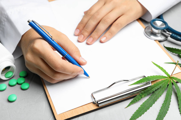 Female doctor with clipboard, pills and hemp leaf at grey table, closeup - Valokuva, kuva