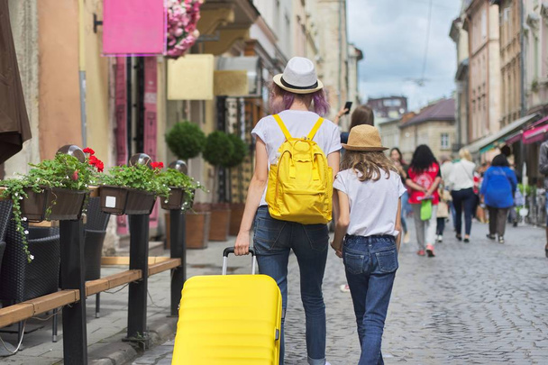 Two girls walking in city with suitcase, back view - Photo, image