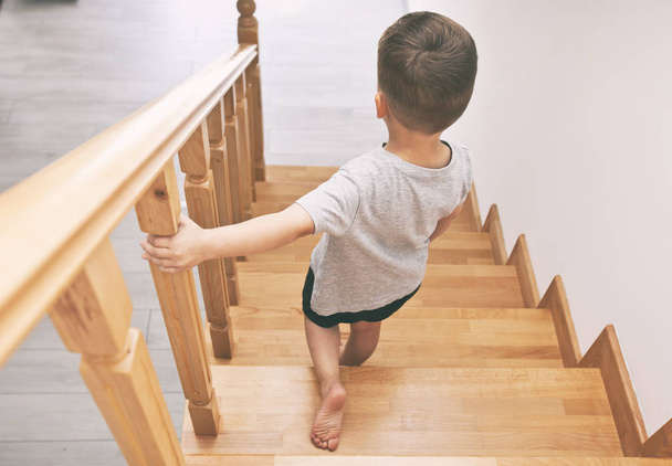 The child is moving down through the wooden stairs in home - Foto, Imagem