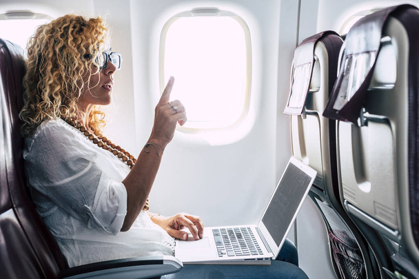 Kaunis nainen matkustaja lentokoneen käyttämällä henkilökohtaista kannettavaa tietokonetta aluksella
 - Valokuva, kuva