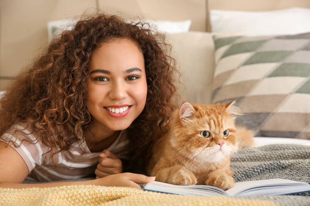 Jonge Afro-Amerikaanse vrouw met schattige kat lezen boek thuis - Foto, afbeelding
