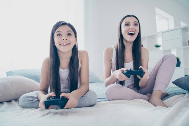 Portrait of two nice-looking beautiful attractive lovely charming cute cheerful cheery glad long haired positive people playing playstation battle amusement in light white interior room indoors - Fotó, kép