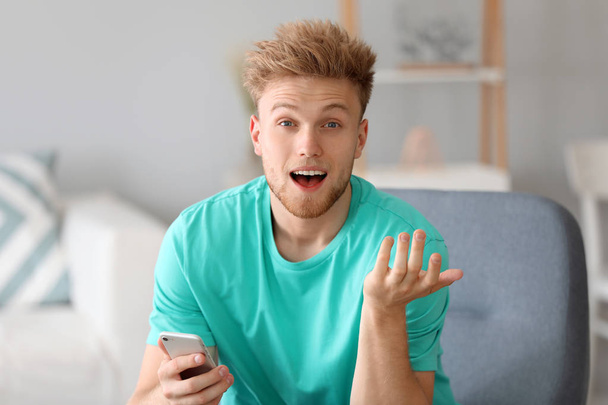 Портрет удивленного мужчины с мобильным телефоном дома
 - Фото, изображение