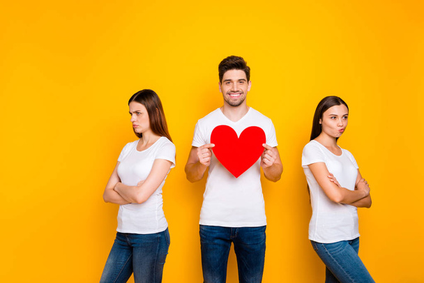 Portrait of one nice attractive cute cheerful cheery guy holding in hands big heart deciding between two offended girlfriends isolated over bright vivid shine yellow background - Foto, imagen