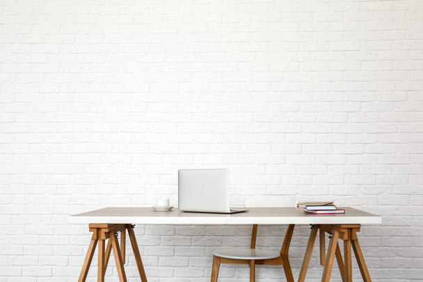 Table with modern laptop and chair near white brick wall - Photo, Image
