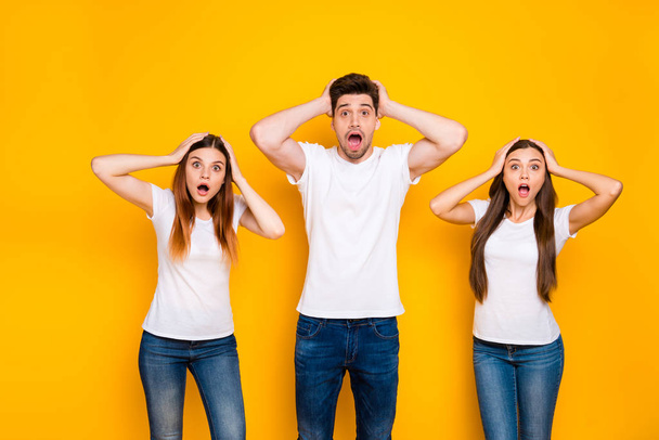 Portrait of astonished buddies touching their heads screaming omg wearing white t-shirt denim jeans isolated over yellow background - Photo, Image
