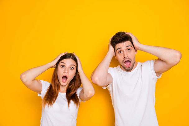 Portrait of astonished people touching their head screaming omg wearing white t-shirt isolated over yellow background - Foto, Imagem