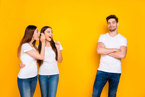 Portrait of chic guy with his arms crossed and excited ladies speaking wearing white t-shirt denim jeans isolated over yellow background - Photo, Image