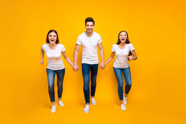 Full length photo of cheerful people holding hands enjoying screaming isolated over yellow background - 写真・画像