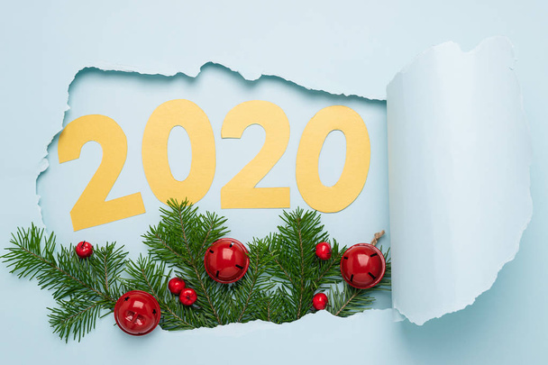 Het symbool van het nieuwe jaar, het cijfer 2020 takken van Fir Tree kerstklokken groot gescheurd papier gat achtergrond blauw - Foto, afbeelding