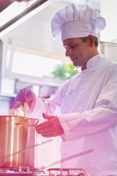 Executive male chef stirring prepared broth before tasting  - Фото, зображення