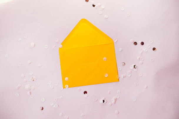 Композиція в стилі мінімалізму порожній жовтий конверт з блискучим декором і бавовняними квітами на рожевому фоні
. - Фото, зображення