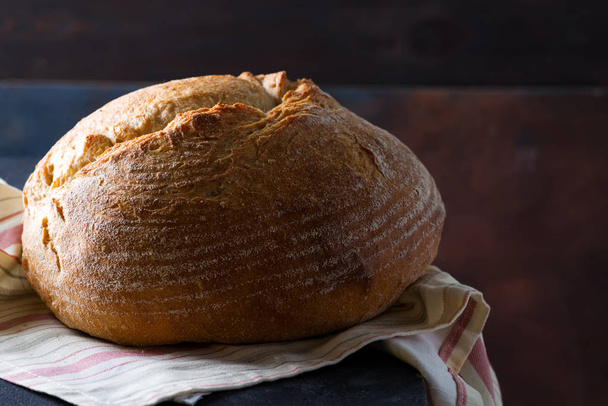Ev yapımı ekmek ekşi hamur, koyu bir arka plan üzerinde bir peçete ile rustik pişmiş ekmek, kopya alanı - Fotoğraf, Görsel