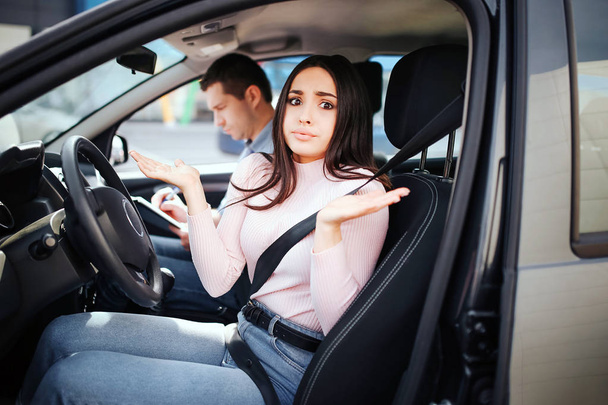 Male auto instructor takes exam in young woman. Sitting together in car. Confused woman look on camera and wave with hands. Busy instructor write. Exam time. - Фото, изображение