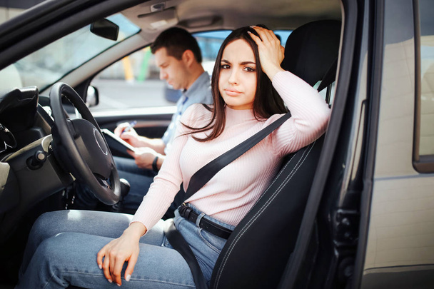 Male auto instructor takes exam in young woman. Bored woman look on camera and pose. Sit together in car. Passed exam. Daylight. - Valokuva, kuva