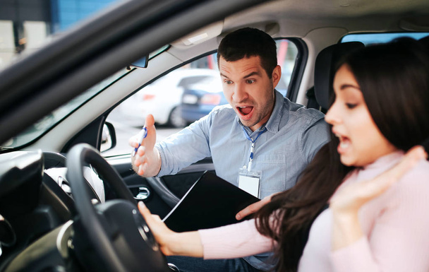 Male auto instructor takes exam in young woman. Screaming on brunette and point with hand. She look down and aegue. Stress and uncomfortable situation. - Φωτογραφία, εικόνα