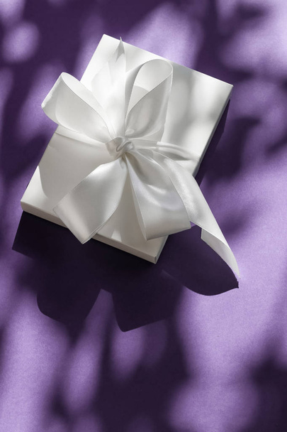 Розкішна святкова біла подарункова коробка з шовковою стрічкою та бантом на фіолетовому
 - Фото, зображення