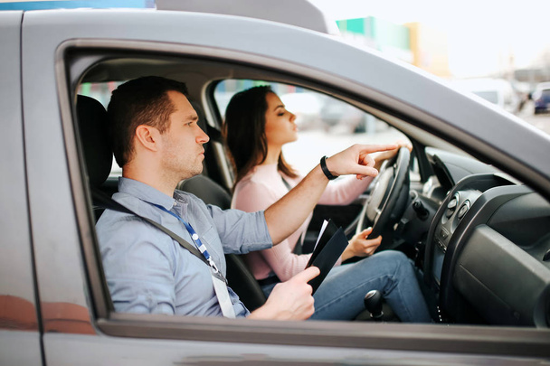 Male auto instructor takes exam in young woman. Careful driving and passing practical test. Instructor help with driving. Young woman pass test with confidence and very careful. - Valokuva, kuva