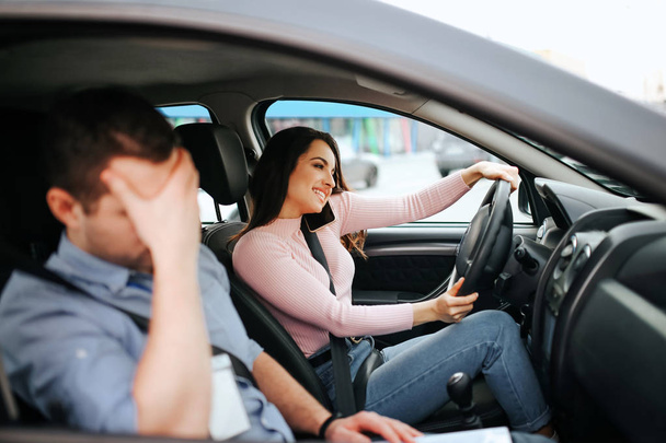 Male auto instructor takes exam in young woman. Shamedguy sit besides careless student that drives car and talk on phone at the same time. - Photo, Image