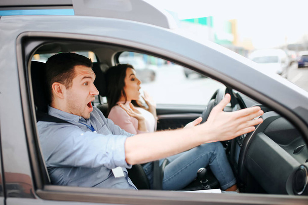 Male auto instructor takes exam in young woman. Scared frightened man point forward with both hands. Female stident driwing without steering wheel. Scared model screaming. - Foto, imagen
