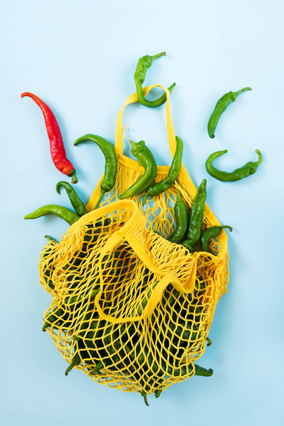 Diseño creativo chiles verdes. Verduras verdes en bolsa de hilo amarillo sobre fondo azul pastel. Montón de pimiento verde llamado frigitelli
 - Foto, imagen