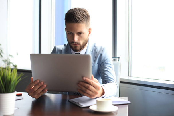 Good looking business man is holding laptop while sitting in the office - Photo, Image