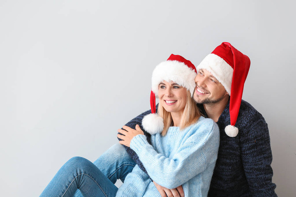 Happy couple in Santa hats on light background - Photo, Image