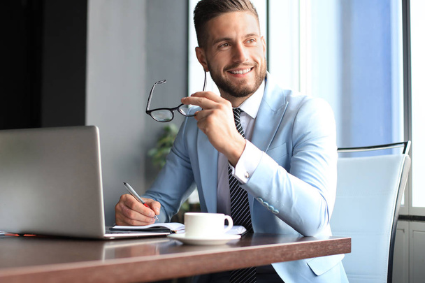 Portrait of happy businessman sitting at office desk, looking at camera, smiling - Foto, Imagen