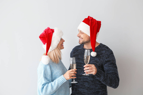 Happy couple in Santa hats drinking champagne on light background - Foto, imagen