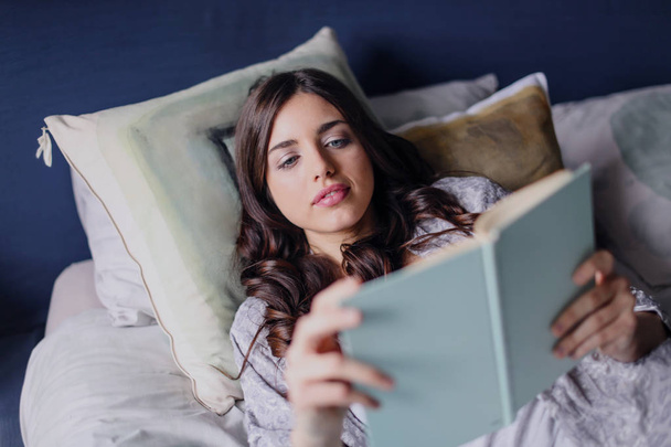 Una chica lee tumbada en la cama
 - Foto, Imagen