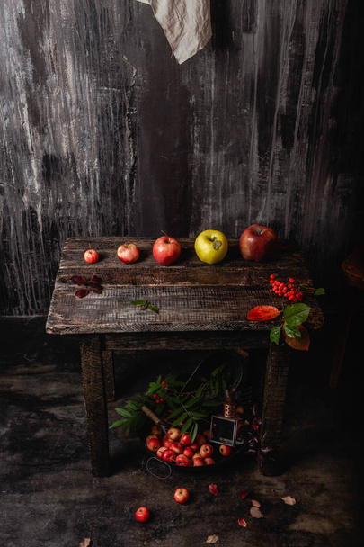 Kolekcja jabłek na drewnianym stole i metalowej patelni z owocami na podłodze w ciemnym pomieszczeniu - Zdjęcie, obraz
